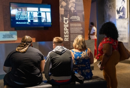 Group of people sitting down watching exhibit screen