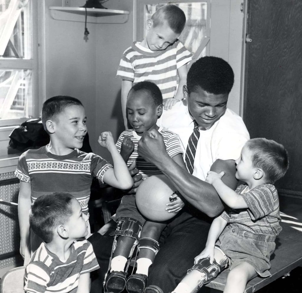 Black and white photo of Muhammad Ali in a shirt and tie with a number of young children in leg braces