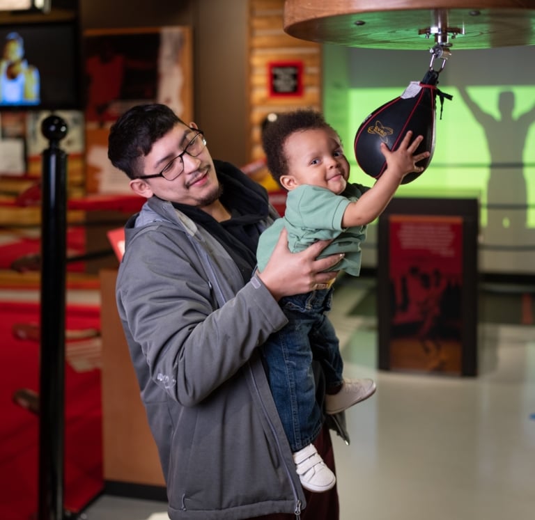 Father and toddler child in the Deer Lake exhibit playing with a speed bag