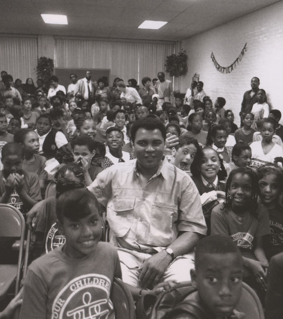 Black and white photo of Muhammad Ali sitting in a room full of students