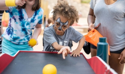 Boy rolls ball in carnival game while girl cheers him on