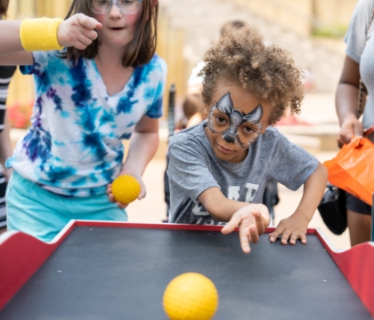 Boy rolls ball in carnival game while girl cheers him on