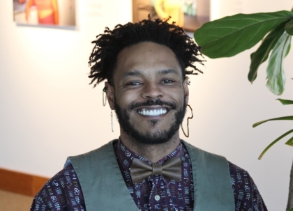 A person smiling with a bow tie, vest, and jewelry