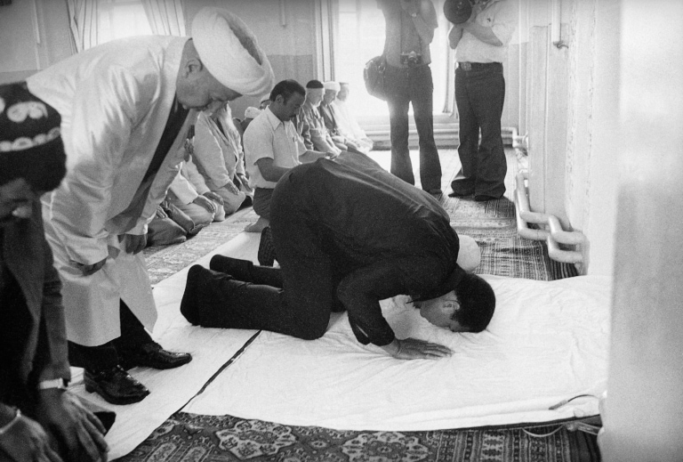 Black and white photo of Muhammad Ali praying with several other Muslim men