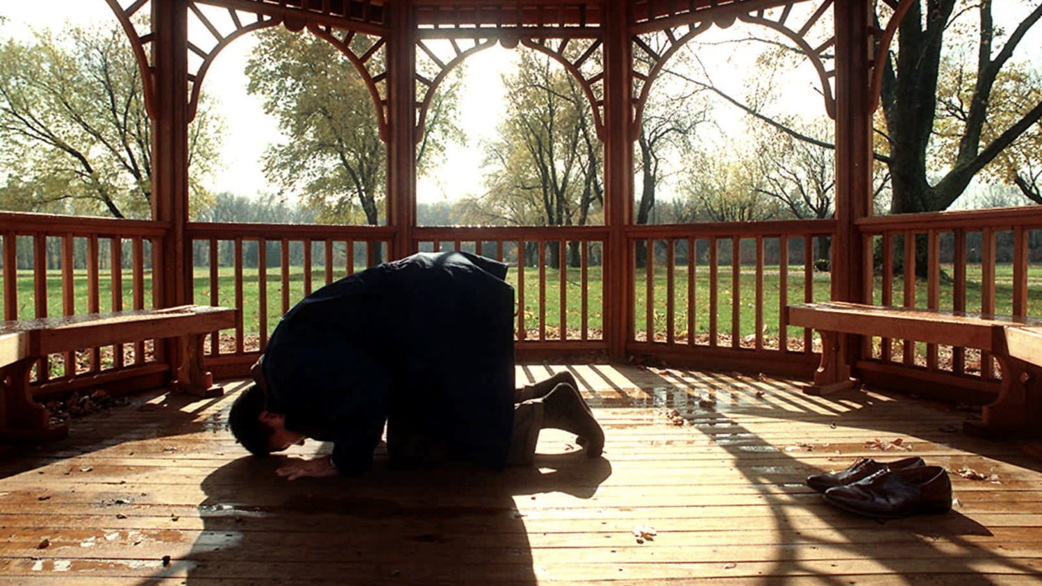 Color photo of Muhammad Ali kneeling and praying in outdoor gazebo