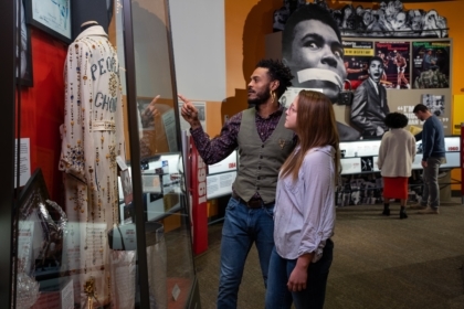 Two people in an exhibit hall pointing at a jumpsuit inside a case