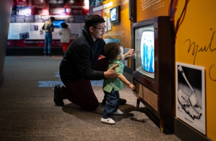 Father and young child kneeling in front of an old television in an exhibit