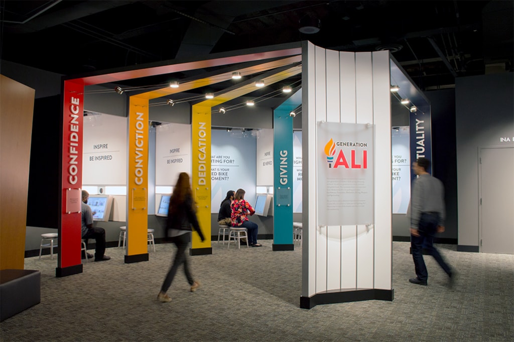 Museum guests sitting in Generation Ali booths while others walk by