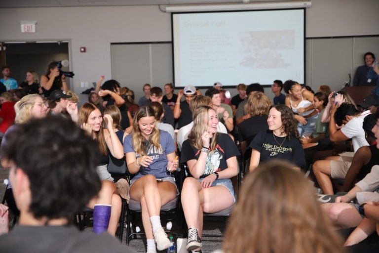 A large room with a projection screen and a large group of seated students