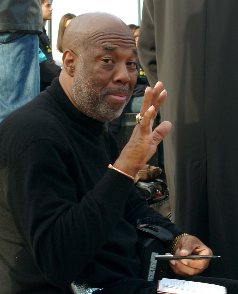 Howard Bingham waves to the camera while sitting down