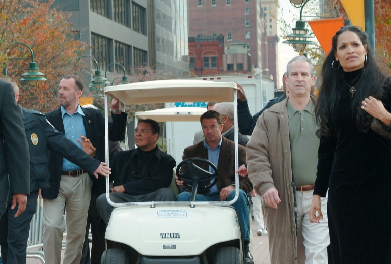 Muhammad Ali getting ride in golf cart while people walk by