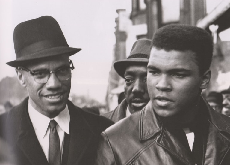 Black and white photo of Muhammad Ali and Malcolm X as young men walking on the street