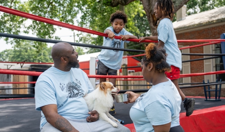 A family of four at the edge of a boxing ring with a a small dog