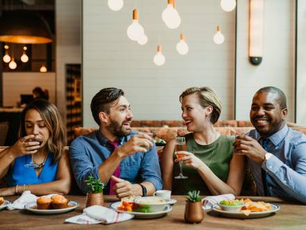 Photo of two couples sitting at a restaurant table with food in front of them and cocktails in hand.