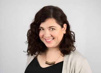 Woman with shoulder-length brown hair, black top, and beige jacket or sweater