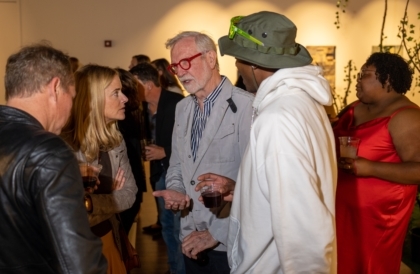 A man with red glasses in a blazer talking to a group of people at an event